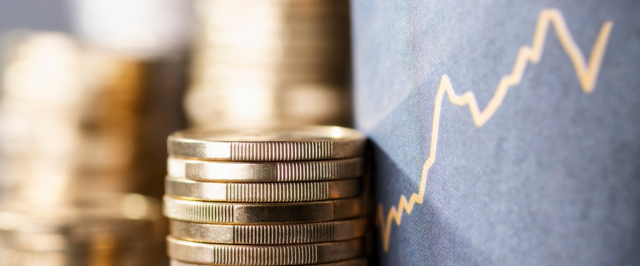 Vier Stapel Münzen sind neben einem grauen Display, auf dem ein Aktienkurs abgebildet ist