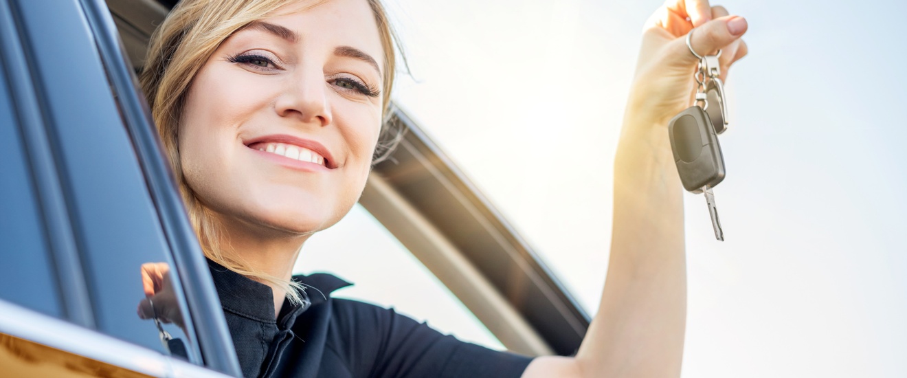 Lächelnde Person aus Autofenster gebeugt hält Autoschlüssel in die Luft