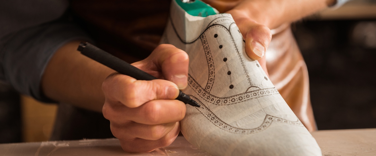 Ein Schuhmacher erstellt einen Prototypen eines Herrenschuhes und zeichnet das Muster auf den Schuh.