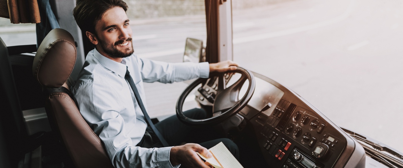 Lächelnde Person an Lenkrad eines Autobusses sitzend nimmt Papier anderer Person entgegen