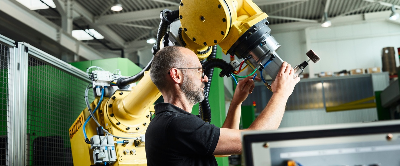 Ein Mann justiert einen Roboterarm in einer Werkhalle