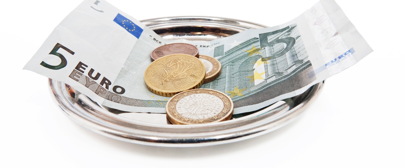 Nahaufnahme eines runden, kleinen Metalltellers, auf dem eine Rechnung ein Fünf-Euroschein und ein paar Münzen sind