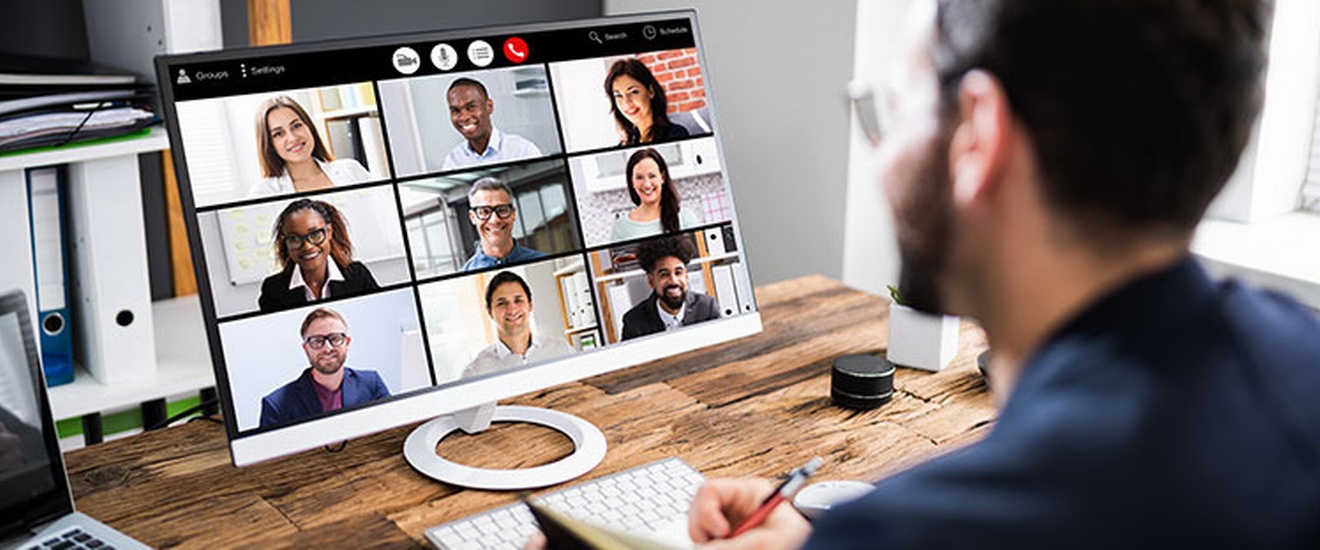 Person vor Computer sitzend, mehrere lächelnde Personen am Bildschirm