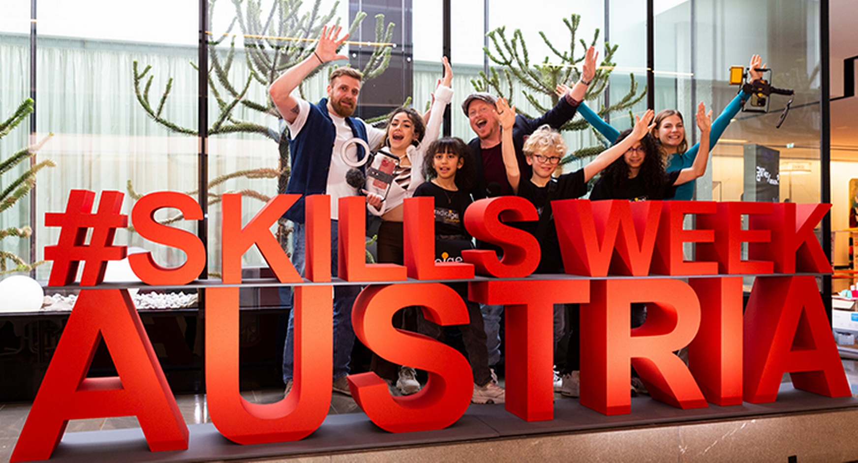 Gruppe winkender Personen vor rotem Schriftzug Skills Week Austria