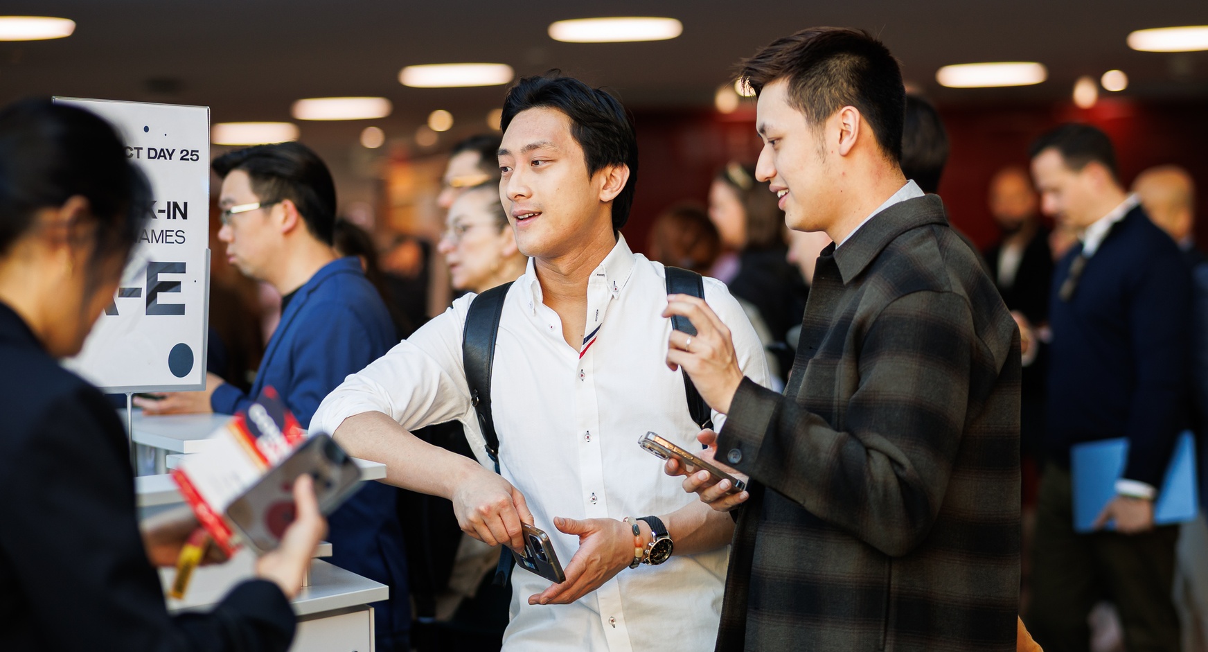 Fokus auf zwei Personen in einer Menschenmasse, die am Check-In-Schalter eines Events miteinander sprechen