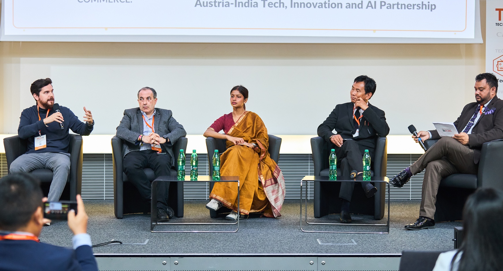 Menschen sitzen nebeneinander auf Sesseln auf einer Bühne 