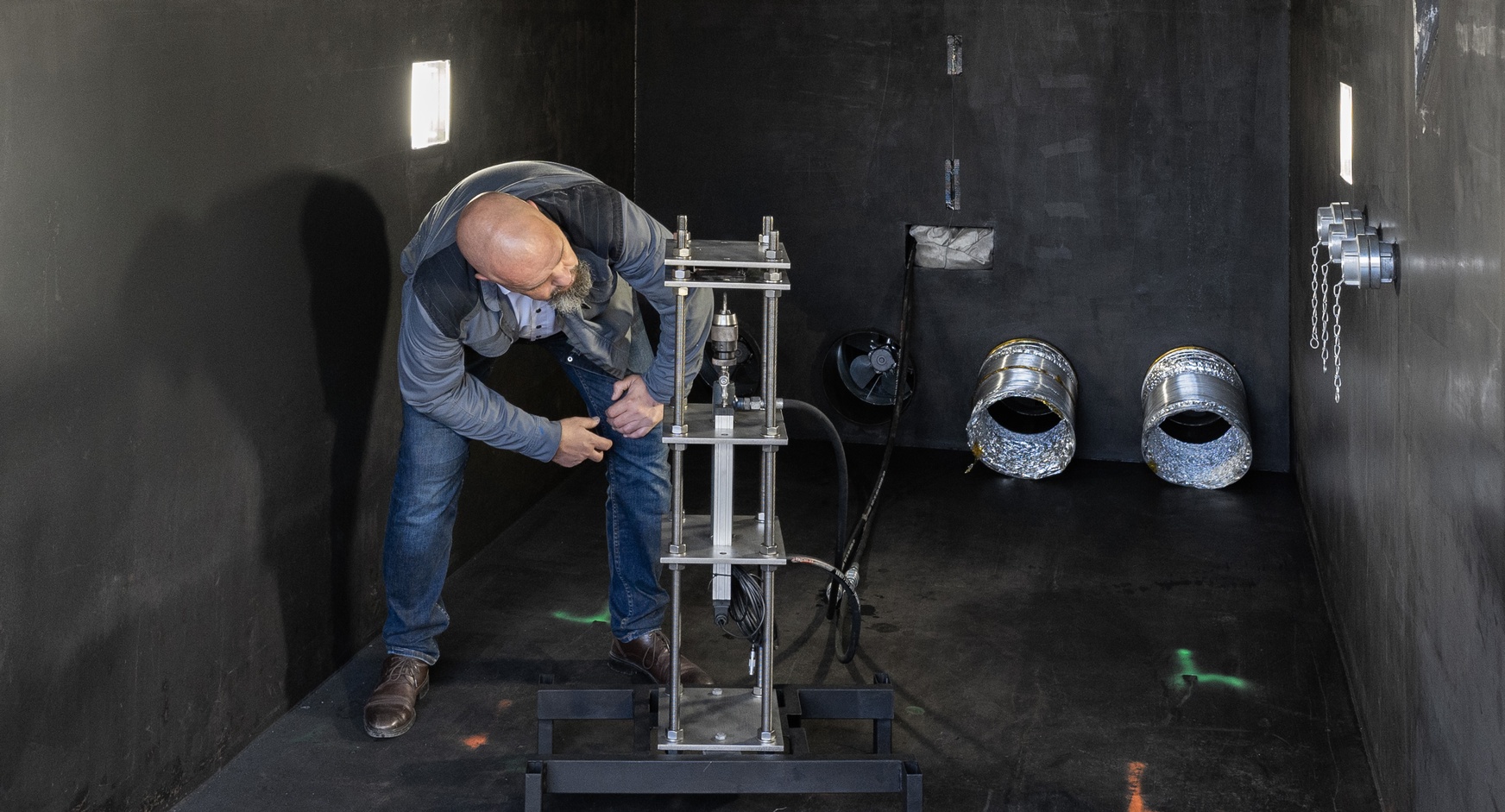 Schwarze Testkammer, eine bärtige Person begutachtet eine Batterie