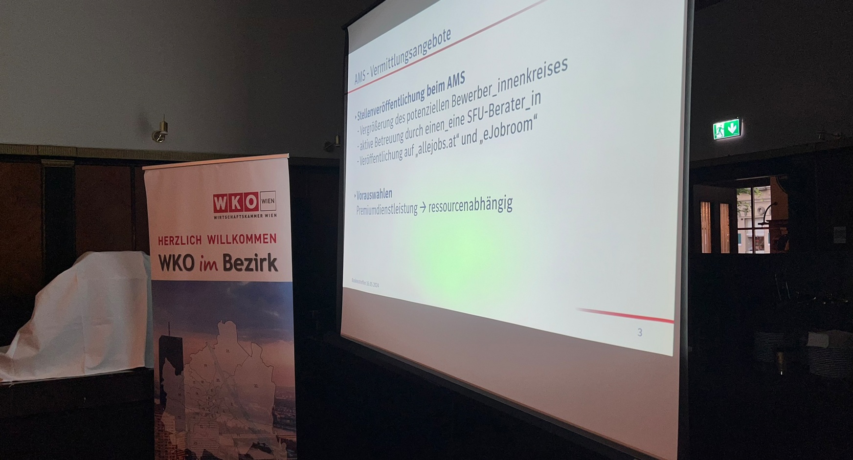 Rollup mit dem Wirtschaftskammer Wien Logo und dem Schriftzug Herzlich Willkommen WKO im Bezirk neben großer Videowall