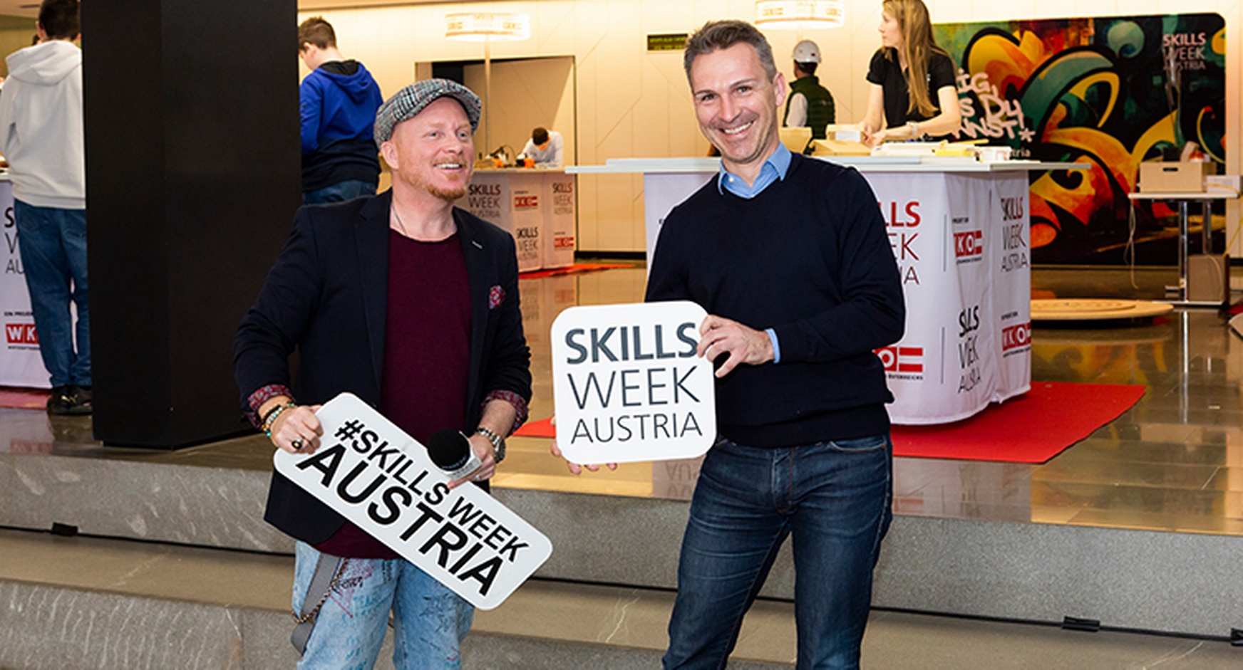 Zwei lächelnde Personen halten Schilder mit Schriftzug Skills Week Austria in Händen