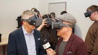 Zwei Personen mit VR-Brillen im Fokus, eine hält Mikrofon in Richtung anderer