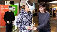 Person hilft anderer Person, die VR-Brille trägt, im Hintergrund weitere Person mit VR-Brille
