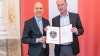 Bundesminister Martin Kocher (l.) überreicht an Joachim Tiefenbacher (r.) die Urkunde zum 
