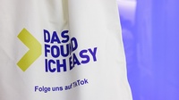 Naufnahme einer weißen Jutetasche vor violett-floriszierendem Hintergrund. Auf der Tasche steht der Schriftzug Das found ich easy Folge uns auf TikTok