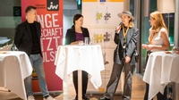 Zu sehen sind Personen, eine davon hat ein Mikrofon in der Hand. Im Hintergrund sind Roll-ups, auf einem steht "Junge Wirtschaft".