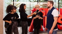Drei Kinder interviewen erwachsene Person, ein Kind hält Mikrofon