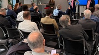 Personen sitzen während einer Veranstaltung im Publikum und hören zu.