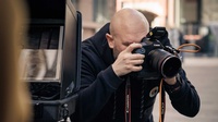 Man sieht den Fotografen Freddy Billqvist bei der Arbeit, er macht mit einer Fotokamera gerade ein Foto von jemandem. Es ist eine Nahaufnahme und man sieht nur den Fotografen auf diesem Bild