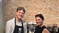 Zwei Personen stehen vor einer Espressomaschine und Kaffeemühlen in einer Kaffeerösterei oder Barista-Schulung. Eine Person trägt eine Schürze mit Corretto-Coffee-Logo, die andere hält einen Siebträger in der Hand. Im Hintergrund ist eine Backsteinwand zu sehen.