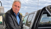 Mann tankt Auto an Tankstelle in Österreich, grauer Himmel, Bäume im Hintergrund.