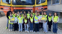 Schülergruppe mit Warnwesten und Plakaten vor einem gelben LKW in Österreich.