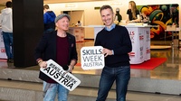 Zwei lächelnde Personen halten Schilder mit Schriftzug Skills Week Austria in Händen