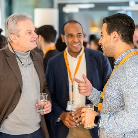 Zu sehen sind Personen bei einem Event, die sich unterhalten und Gläser mit Flüssigkeiten in der Hand halten.