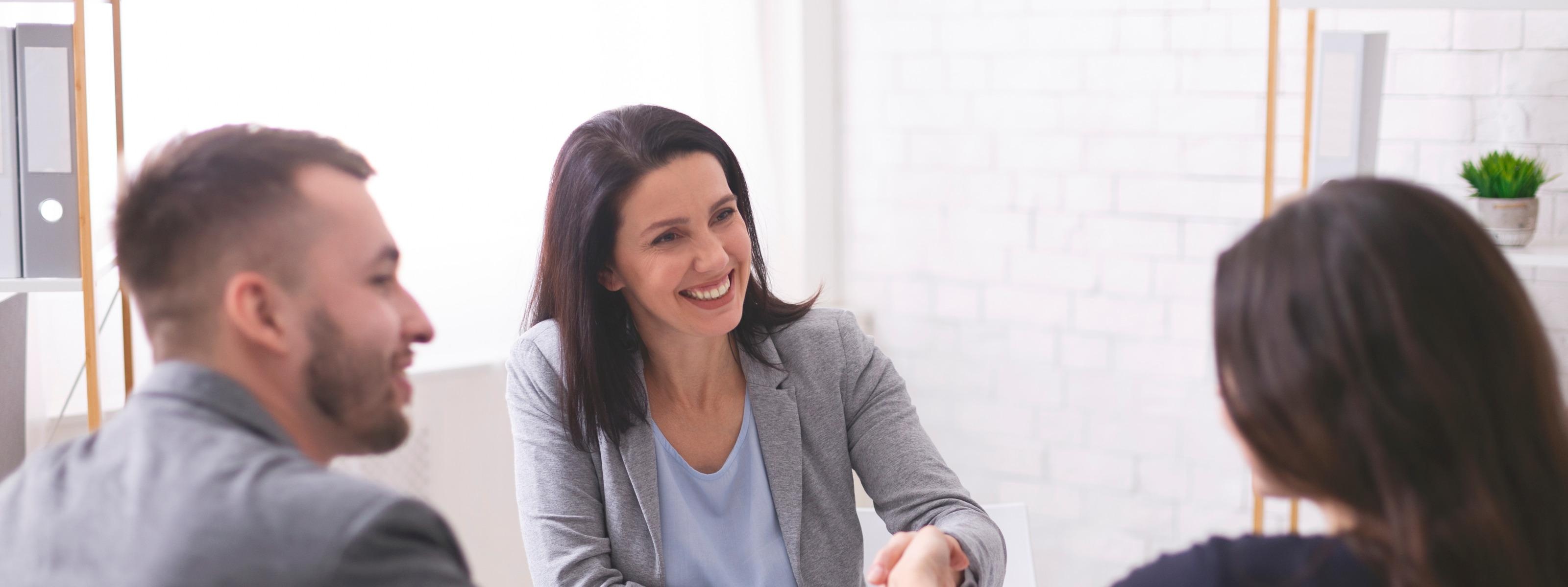 Drei Personen sitzen an Tisch, zwei schütteln sich die Hand