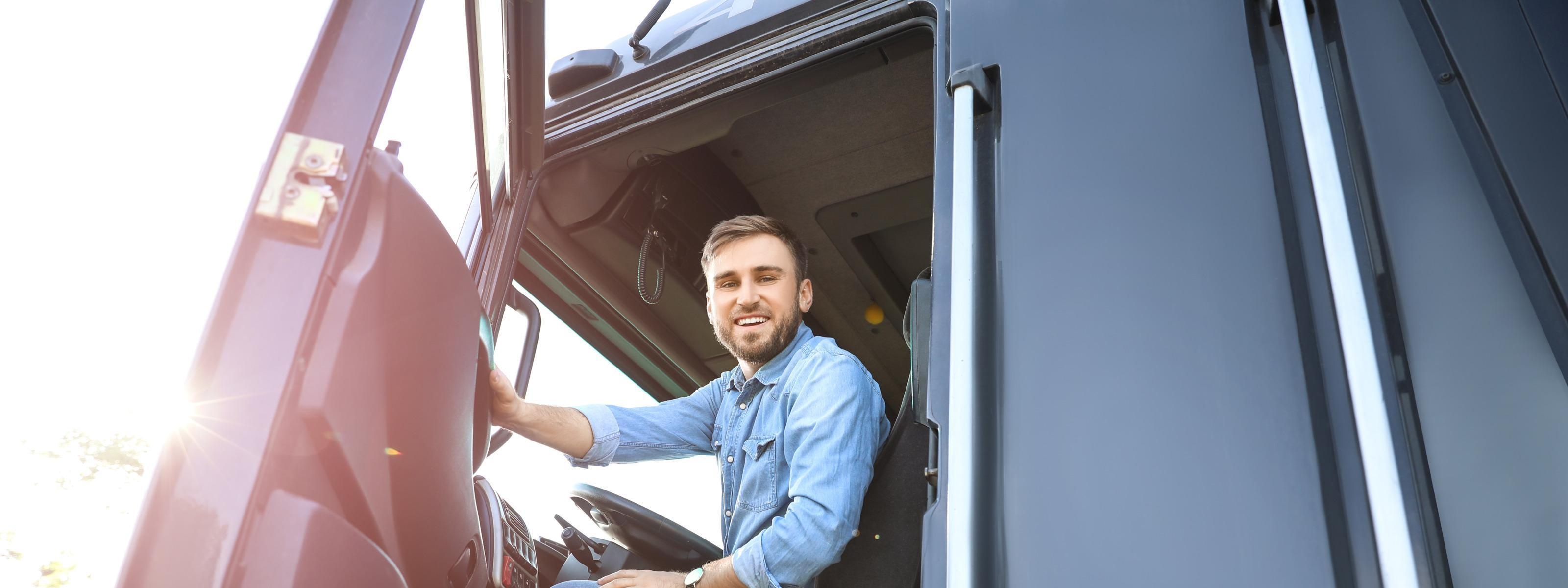 Lächelnde Person sitzt hinter Steuerrad eines LKWs und blickt aus geöffneter Türe