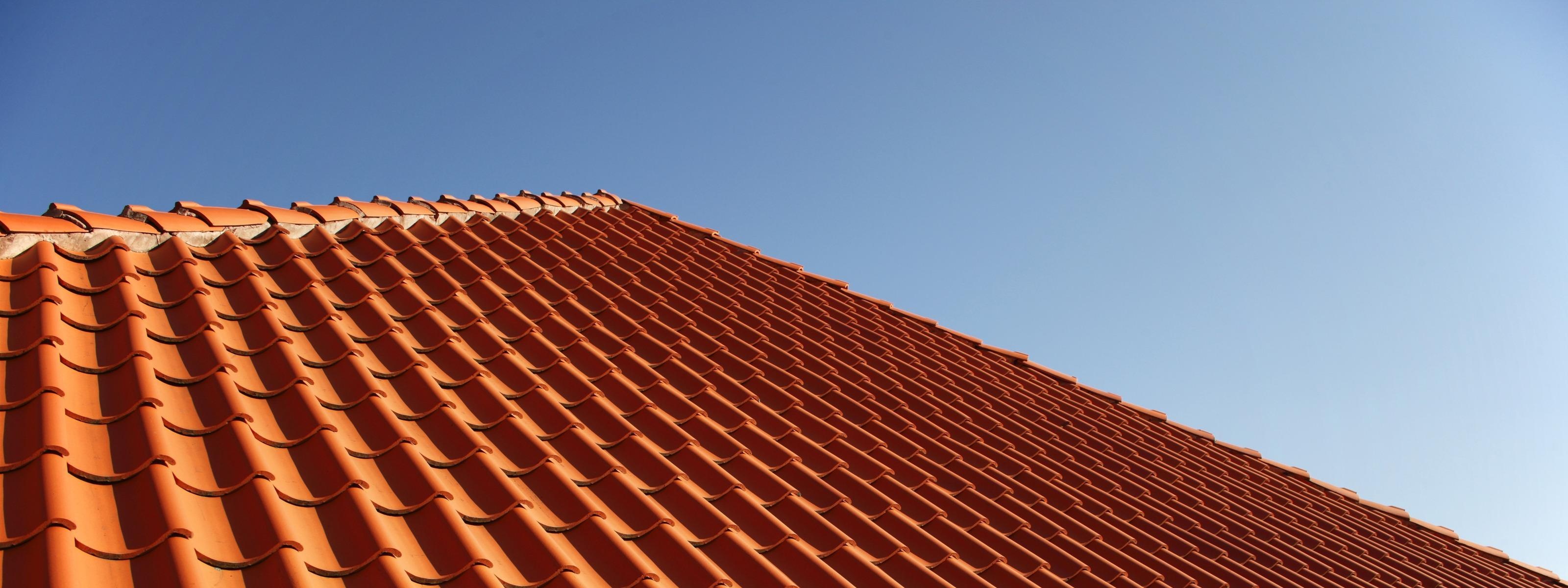Detailansicht eines Daches mit rotorangen Dachschindeln, blauer Himmel im Hintergrund