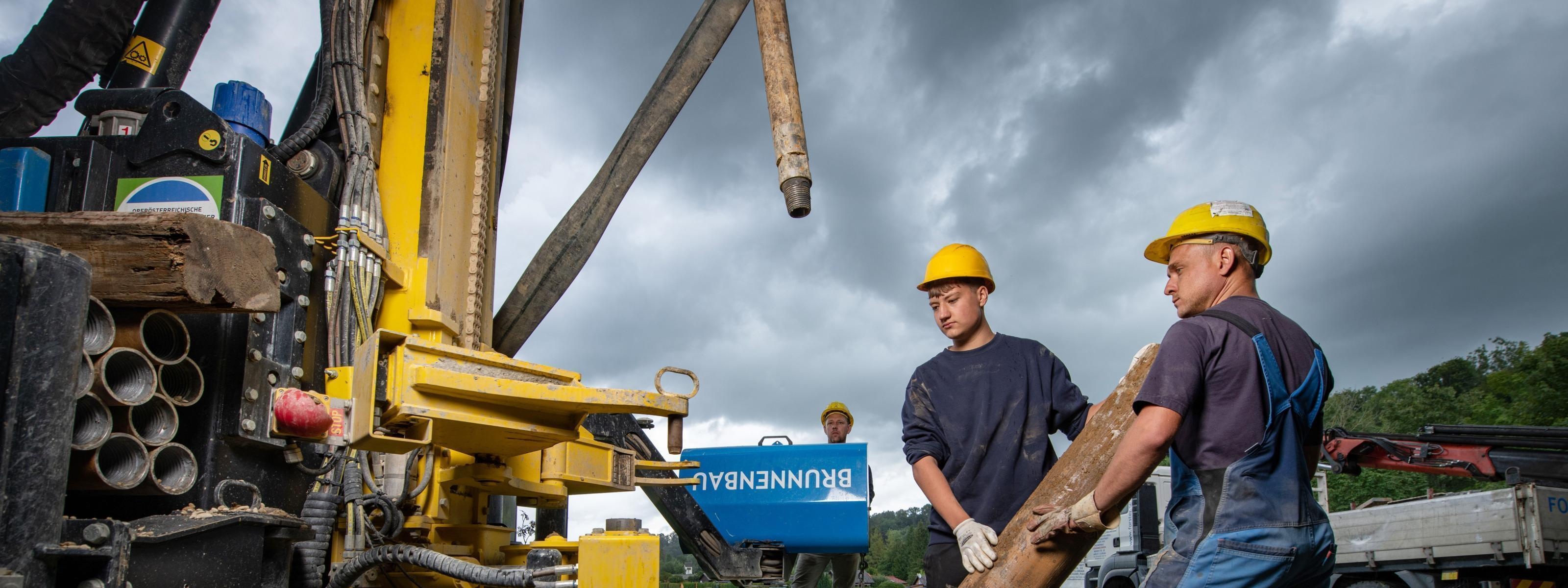Personen in Arbeitskleidung mit gelbem Schutzhelm führen Brunnenbauarbeiten gemeinsam mit Unterstützung eines Baggerkrans durch