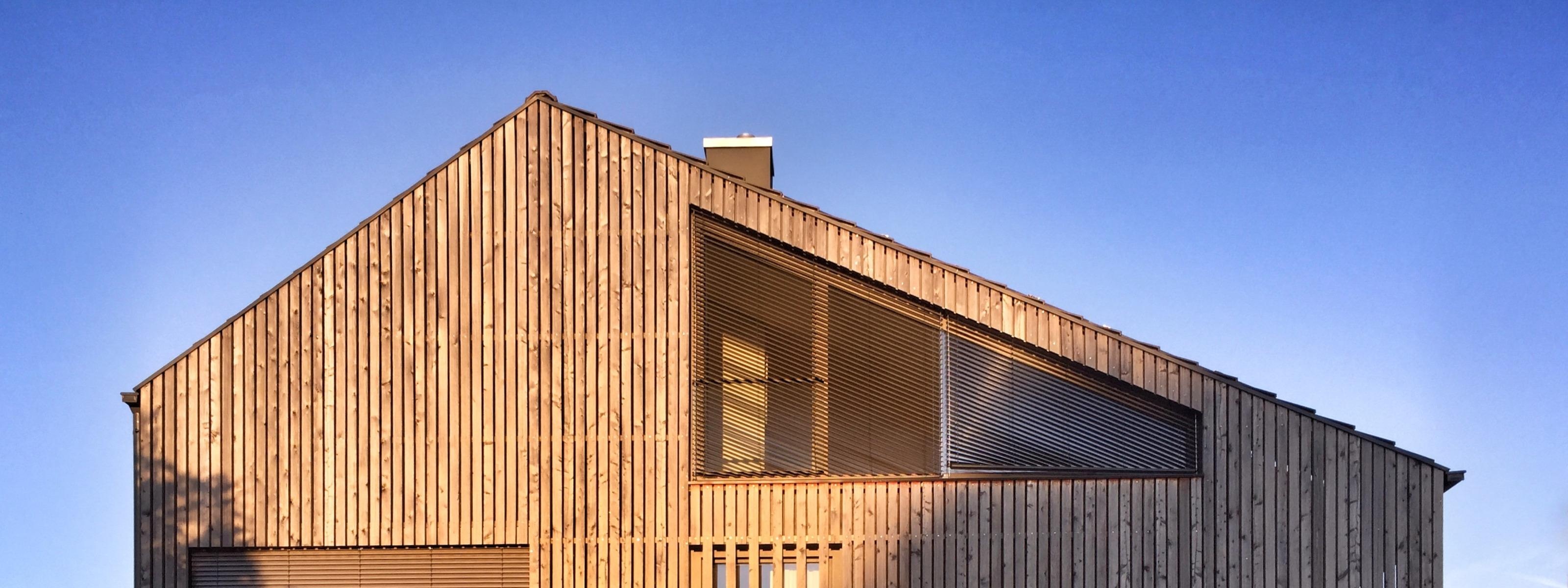 Haus mit Holzverschalung in Sonnenlicht, im Hintergrund blauer Himmel
