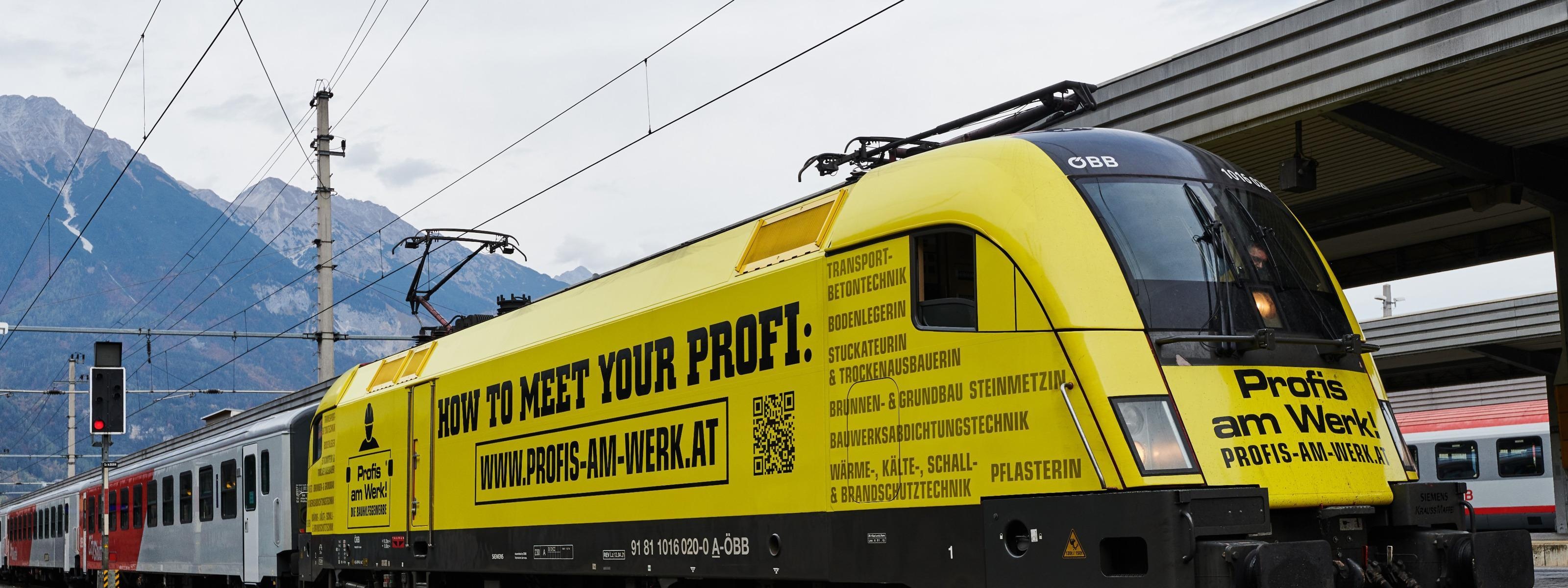 Gelber Zug mit Beschriftung auf Bahngleis neben Bahnsteig stehend