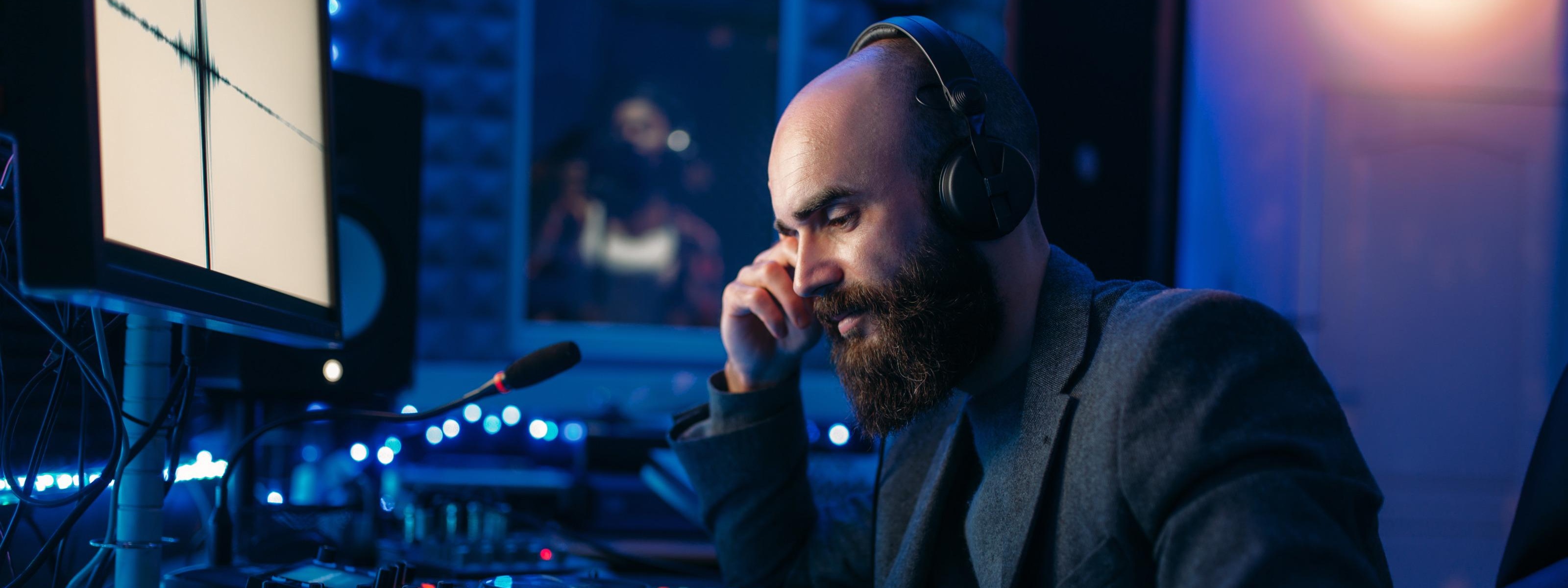 Person mit Bart und Kopfhörern bedient Mischpult