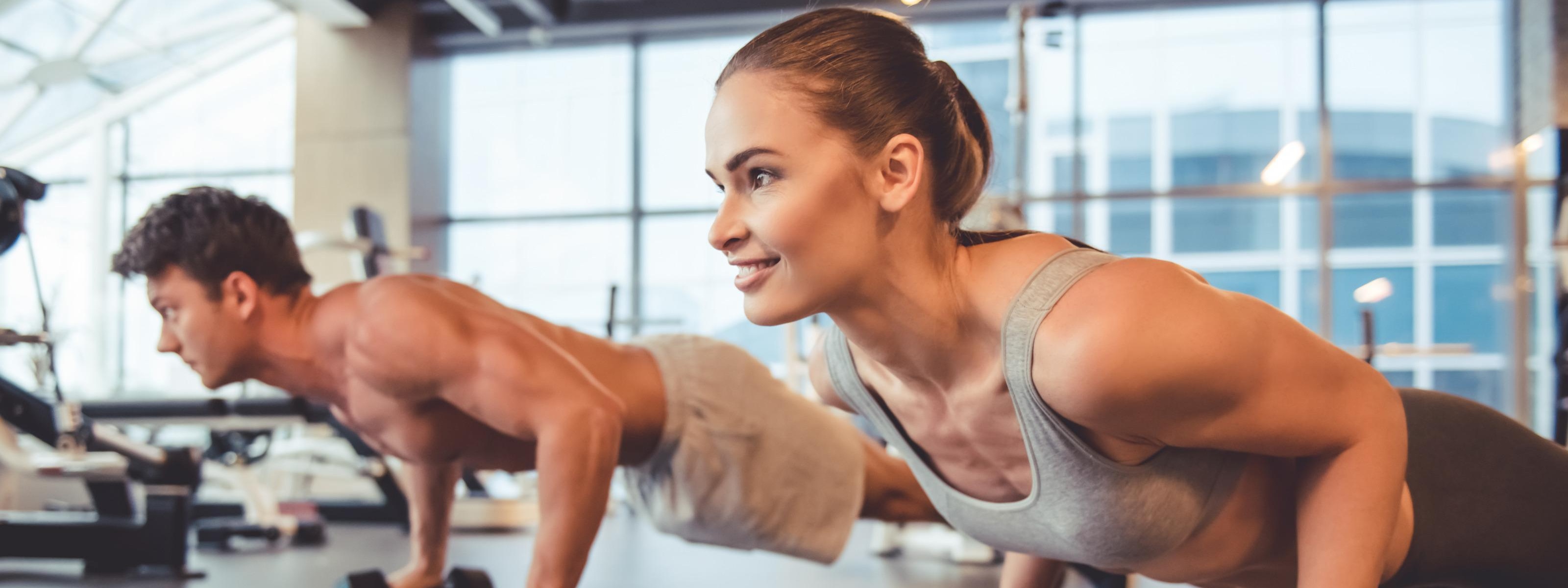 Personen in Sportkleidung trainieren mit einer Hantel und planken in einem Fitnessstudio