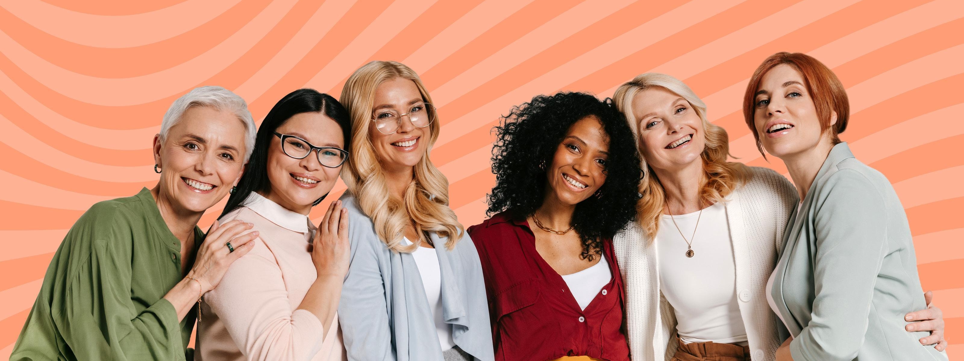 Frauengruppe, die eng nebeneinander stehen. Sie lächeln in die Kamera und wirken freundlich, entspannt und verbunden.<br />
Die Frauen sind unterschiedlich alt – einige wirken jünger, andere älter – und haben verschiedene Hautfarben und bunte Outfits.