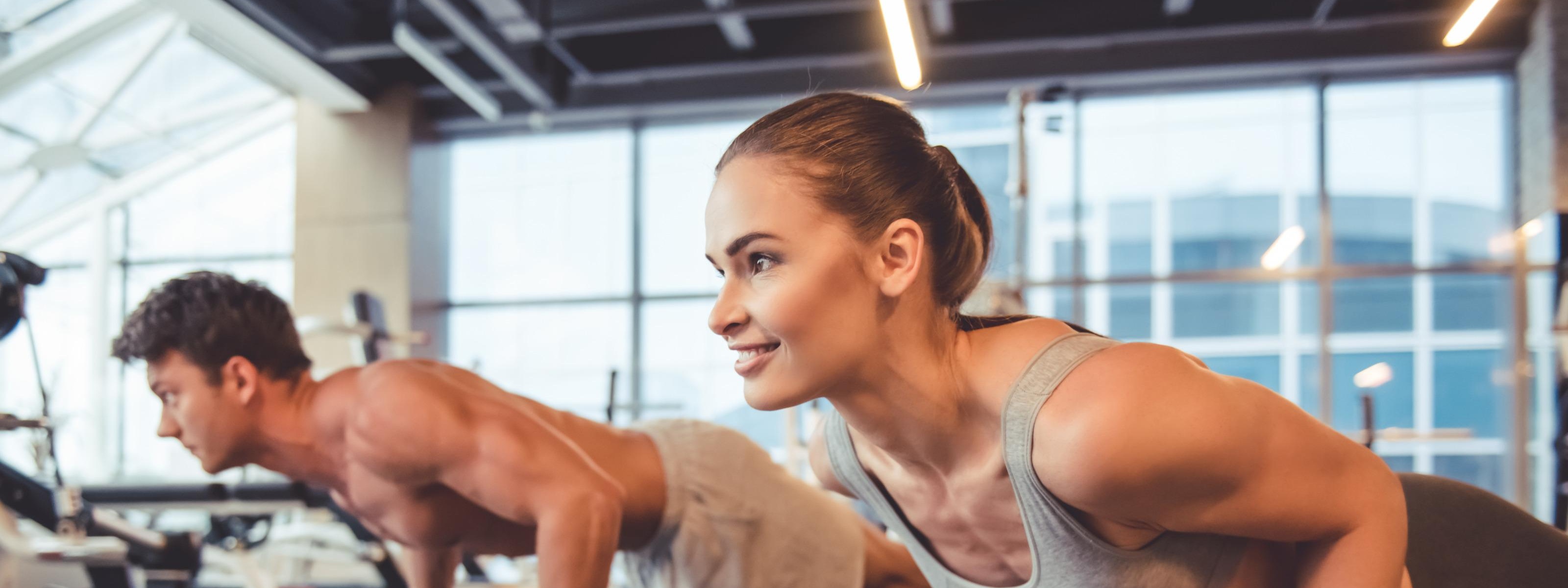 Personen in Sportkleidung trainieren mit einer Hantel und planken in einem Fitnessstudio