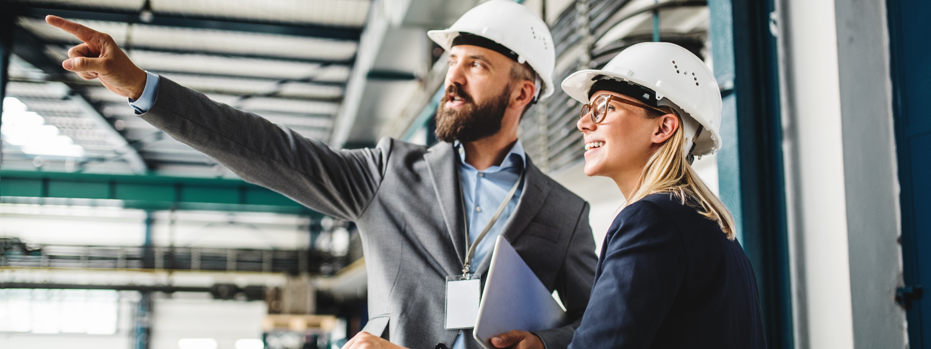 Zwei Personen mit weißen Schutzhelmen blicken in selbe Richtung, in die eine der Personen deutet