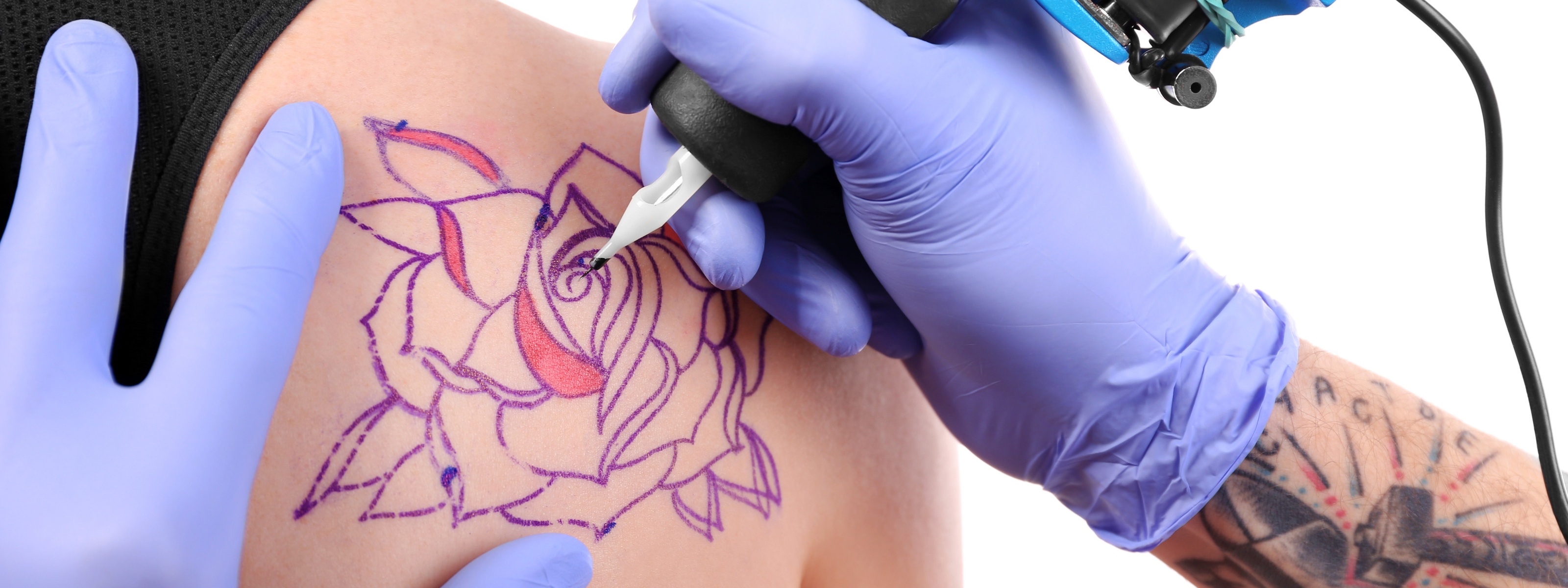 Nahaufnahme von der Erstellung eines Tattoos auf der Schulter einer Person mit einer Tätowiermaschine und lila Handschuhen