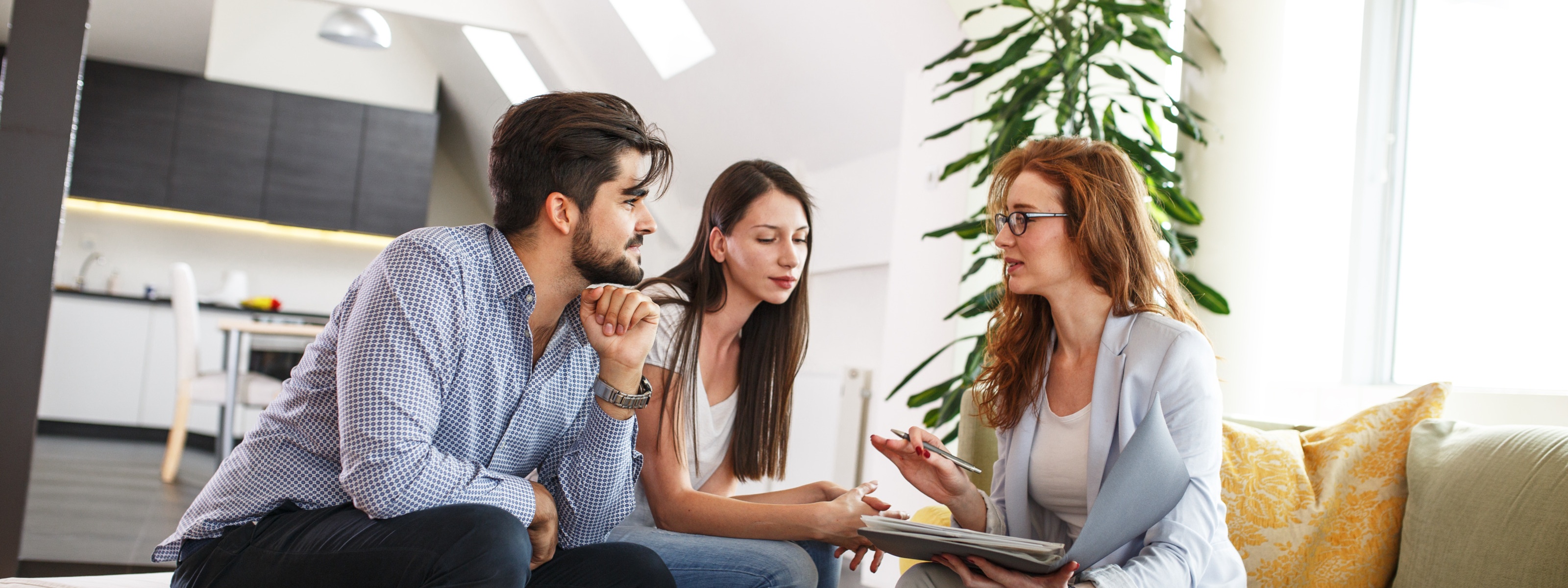 Drei Personen sitzen an Couchtisch in Wohnung und unterhalten sich