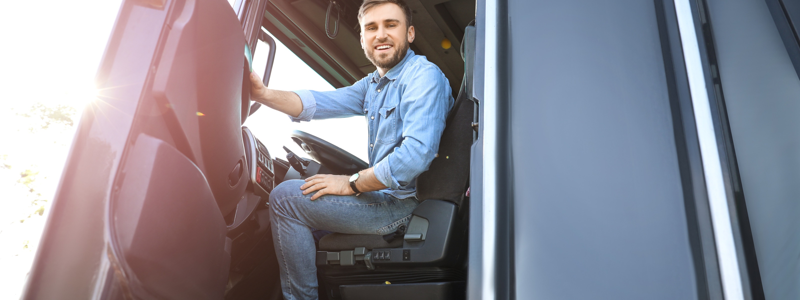 Lächelnde Person sitzt hinter Steuerrad eines LKWs und blickt aus geöffneter Türe