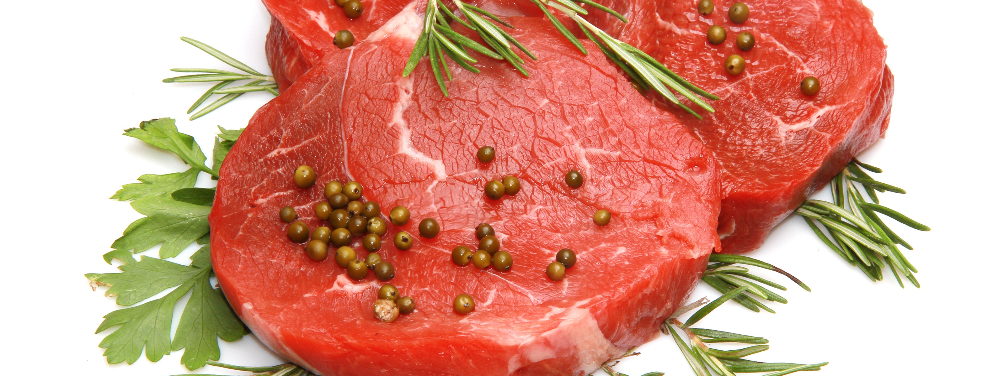 Rohes Fleischstück mit Pfefferkörnern, Rosmarinzweigen und Petersilie auf weißem Hintergrund