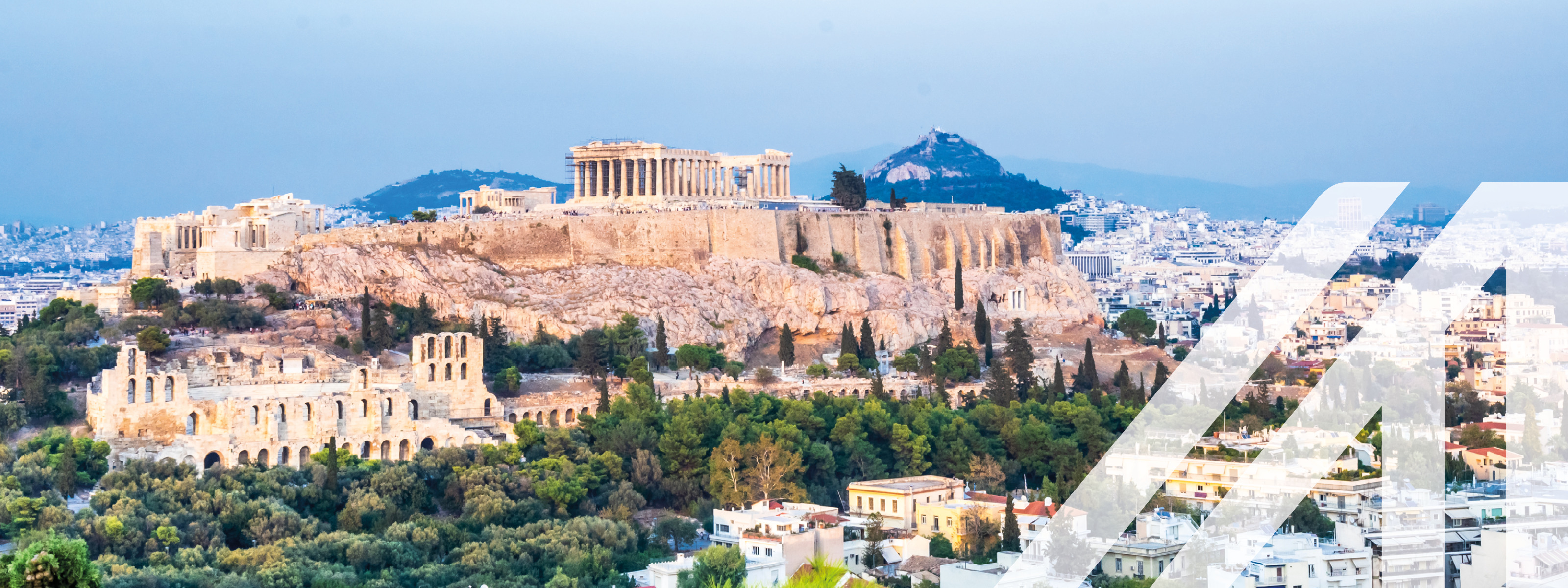 Blick auf die Stadt Athen mit dem Akropolis-Berg, umrandet von Bäumen. Über das Bild wurde ein weißes Austria A gelegt.