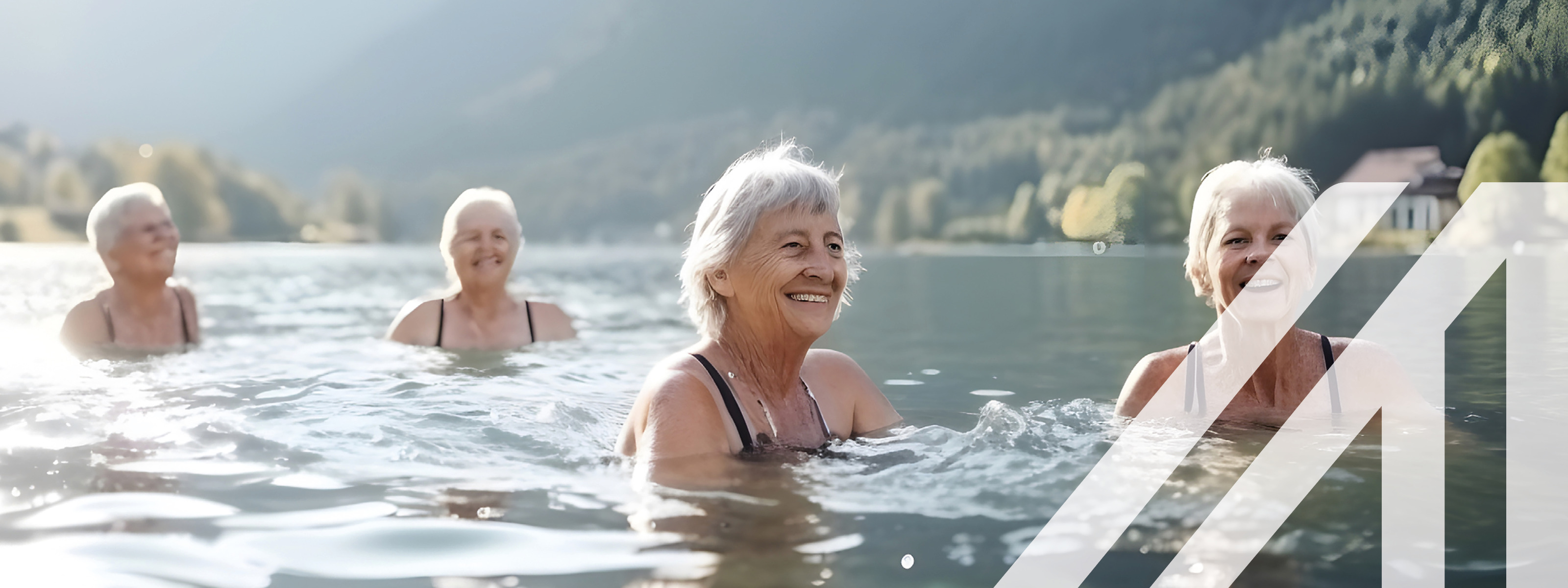 Aktive Seniorengruppe beim Schwimmen im See vor begrünten Bergen im Hintergrund