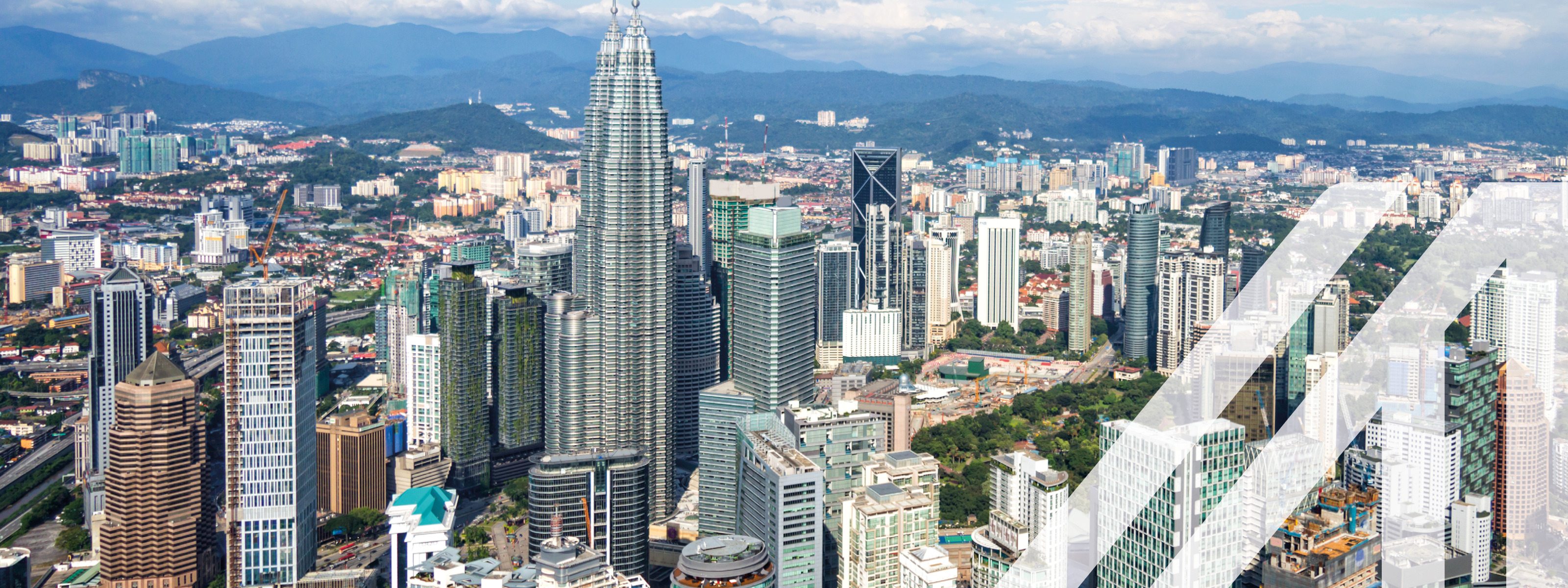 Blick von oben auf die modernen Gebäude von Kuala Lumpur, im Hintergrund erkennt man eine bewaldete hügelige Landschaft