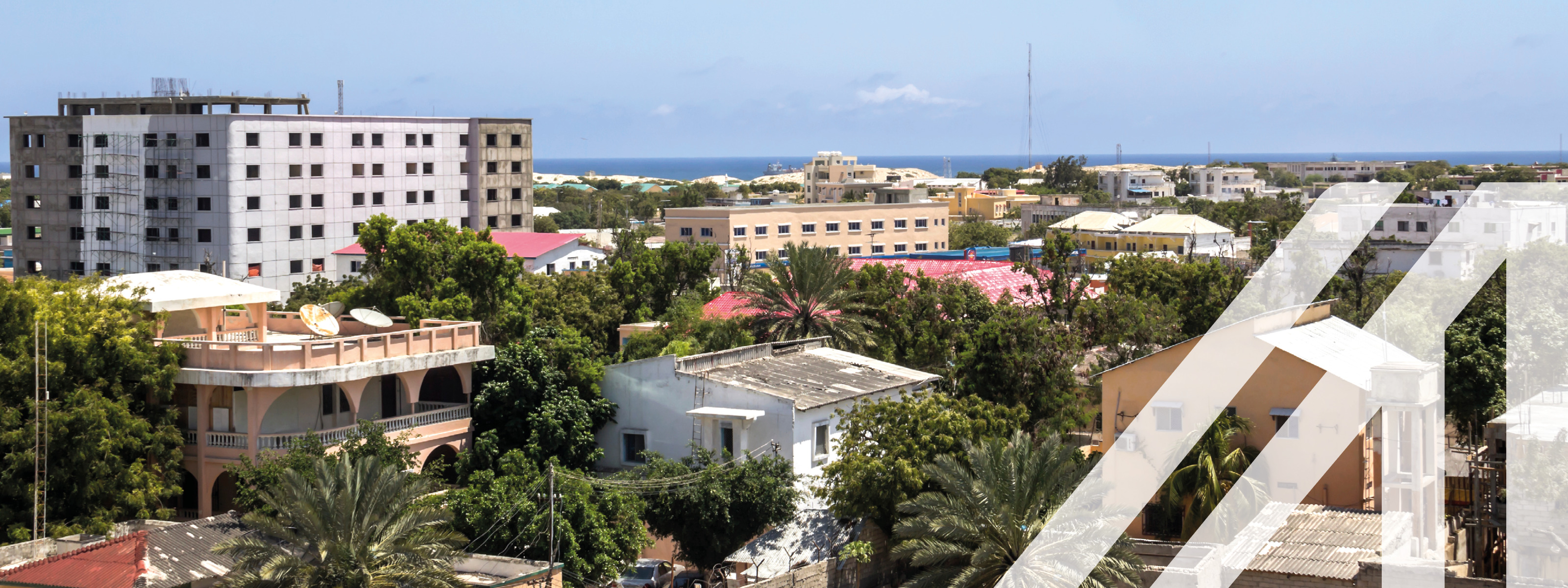 Stadtansicht von Mogadischu, Hauptstadt von Somalia: Zwischen Häusern Bäume, im Hintergrund Meer unter blauem Himmel<br />
