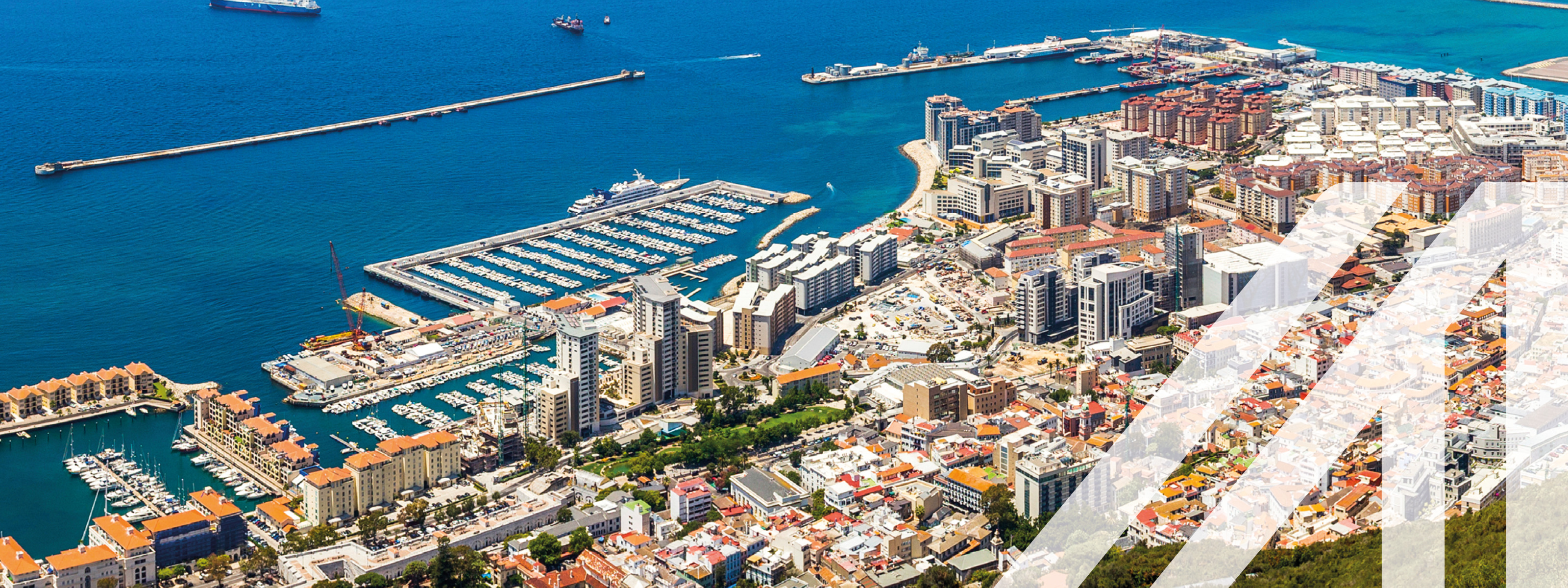 Stadtansicht von Gibraltar: Im Vordergrund steil aufsteigender Bergfels, im Hintergrund Stadtlandschaft mit Hafen umgeben von Meer
