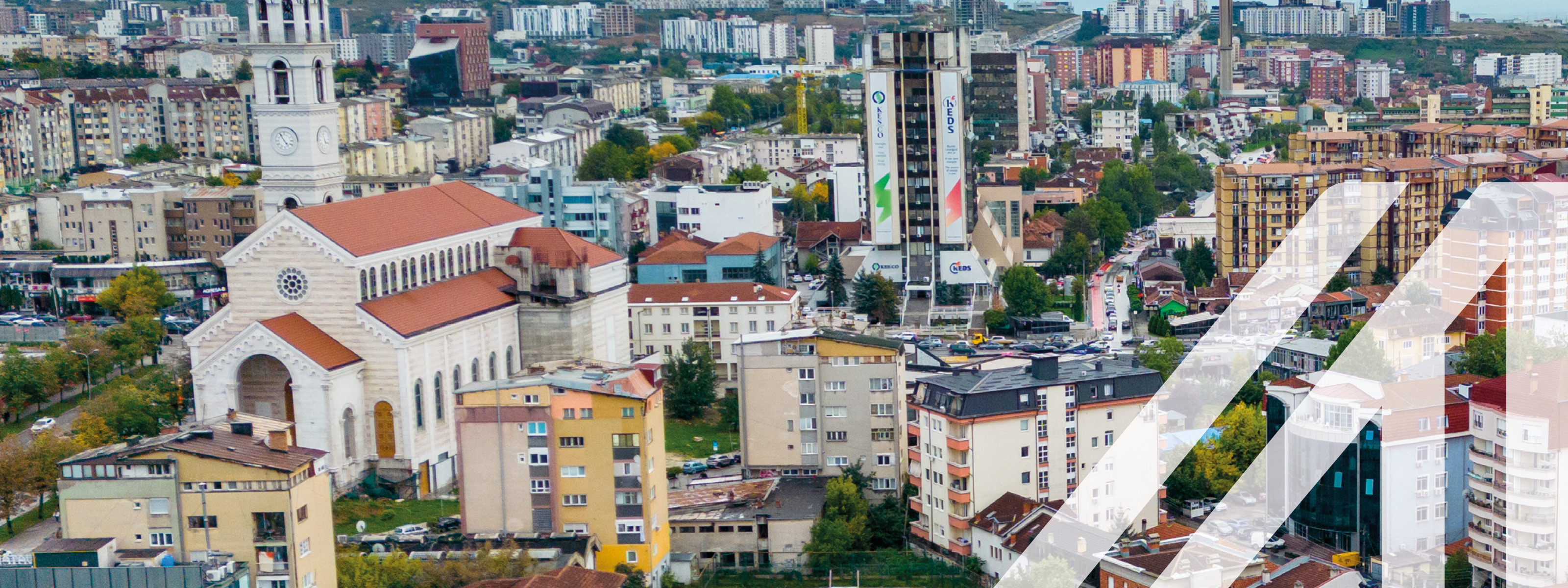 Stadtansicht von Pristina: Bunte Häuser und eine Kirche, im Hintergrund nebelverhangene Bergkette