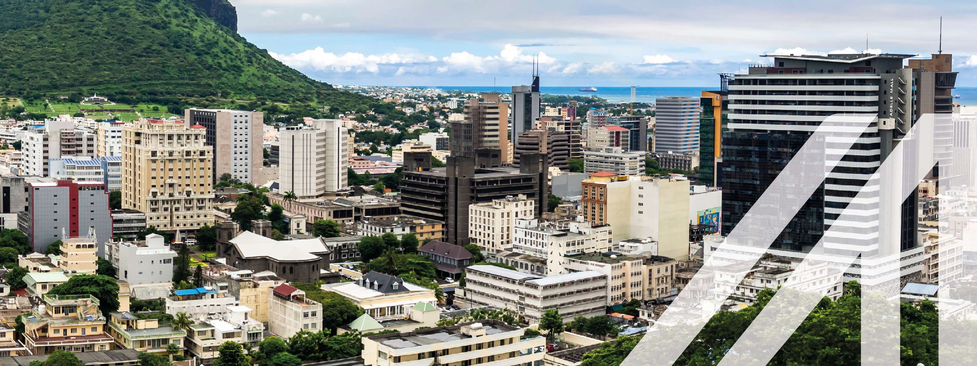 Blick auf die modernen Häuser von Port Louis, Mauritius. Links im Bild erhebt sich ein bewaldeter Hügel, in der ferne erkennt man das Meer.<br />
