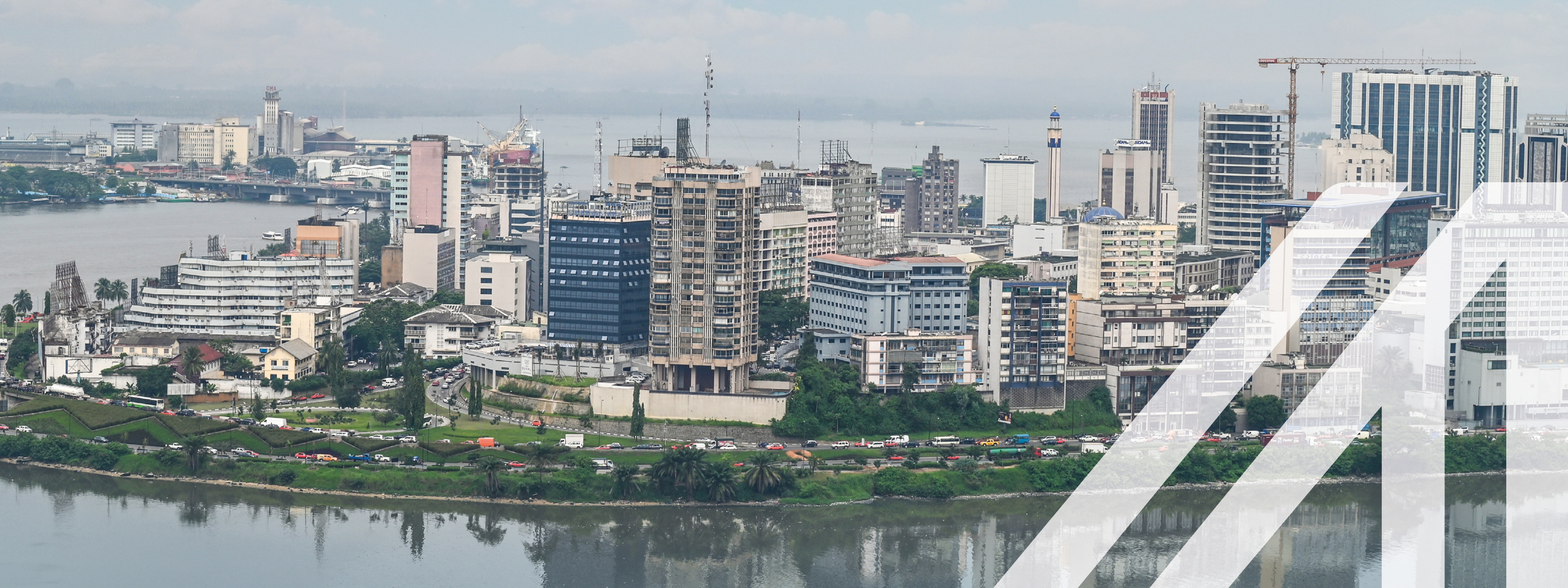 Stadtansicht von Abidjan unter blauem Himmel mit modernen Hochhäusern an einem begrünten Ufer