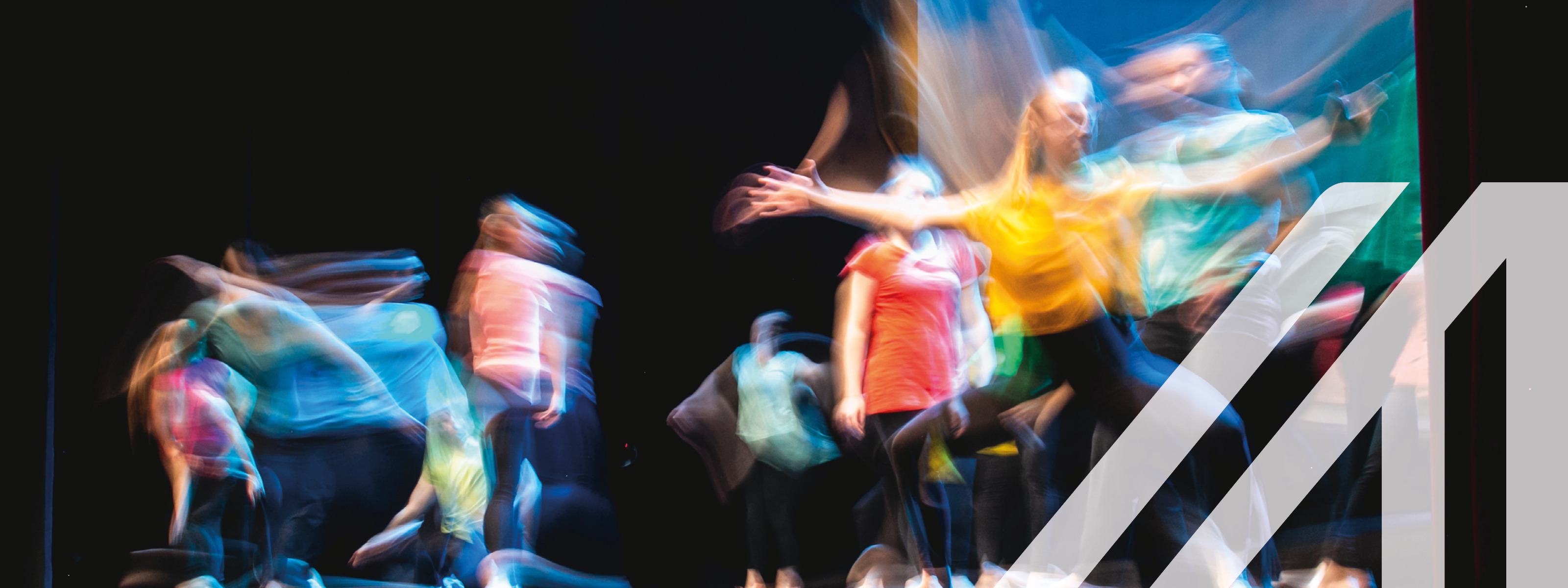 Gruppe von Tänzern in farbigen Kleidern tanzen auf der Bühne in Langzeitbelichtung